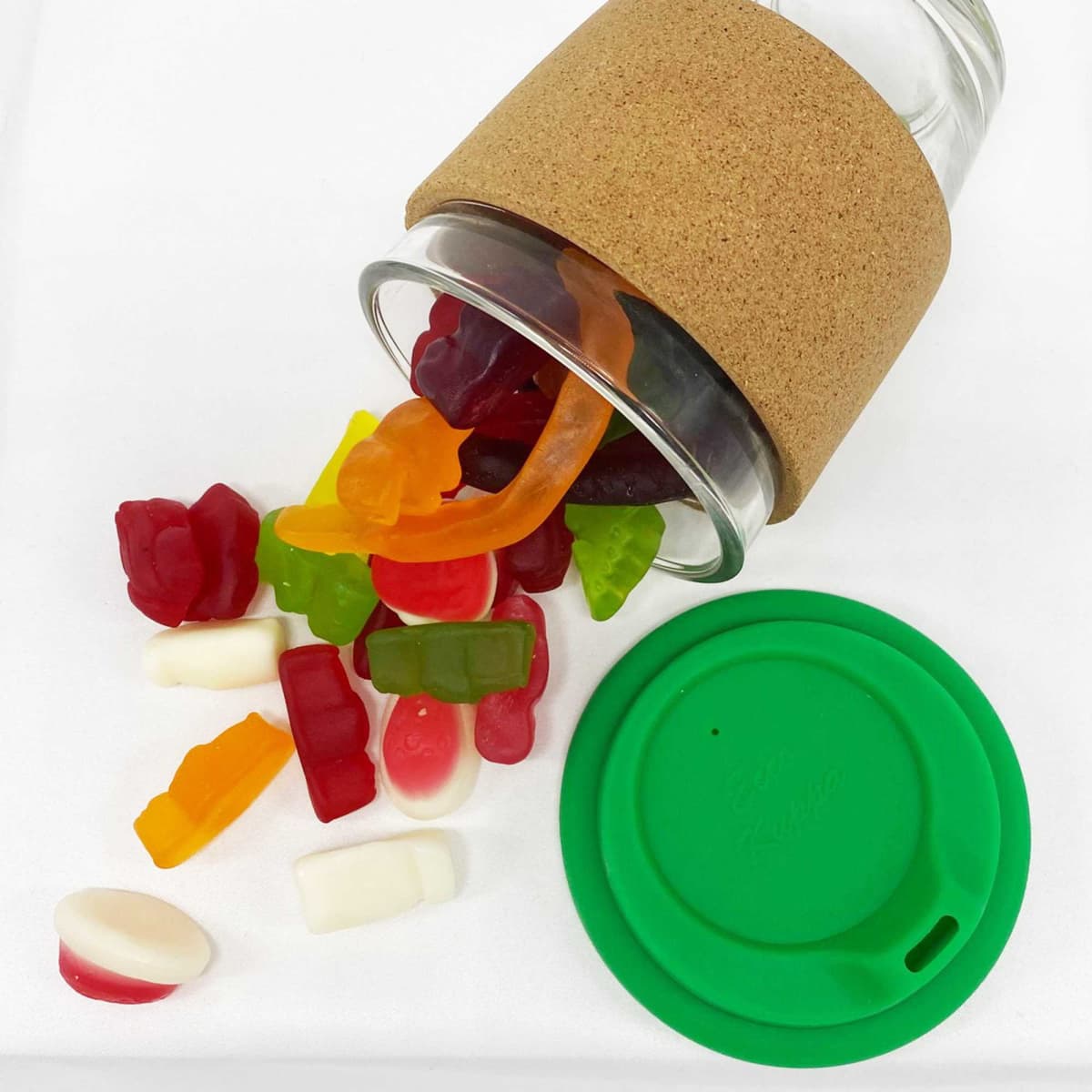 A glass coffee cup with a cork band, filled with colourful mixed lollies in red, green, orange, and yellow.