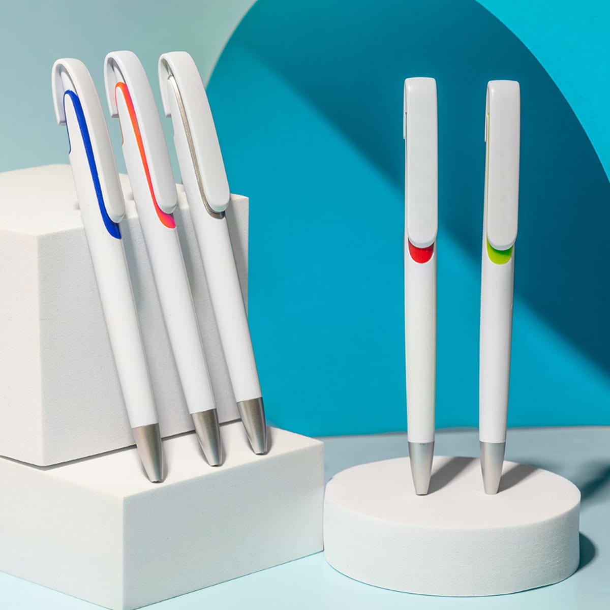 A collection of white plastic pens featuring coloured accents in blue, red, and green, displayed on geometric risers.