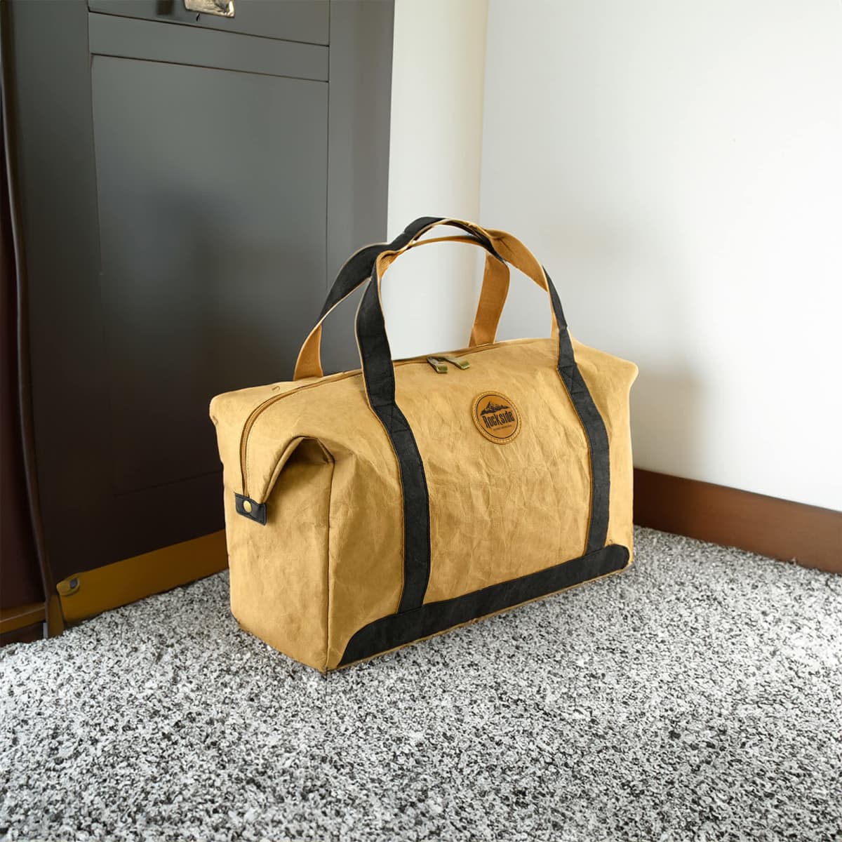 A yellow kraft paper travel bag with black accents, featuring handles and a logo. It rests on a textured surface.