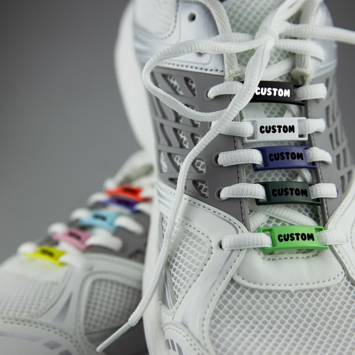 A pair of white sneakers featuring colourful luxury shoelace charms with a custom design.