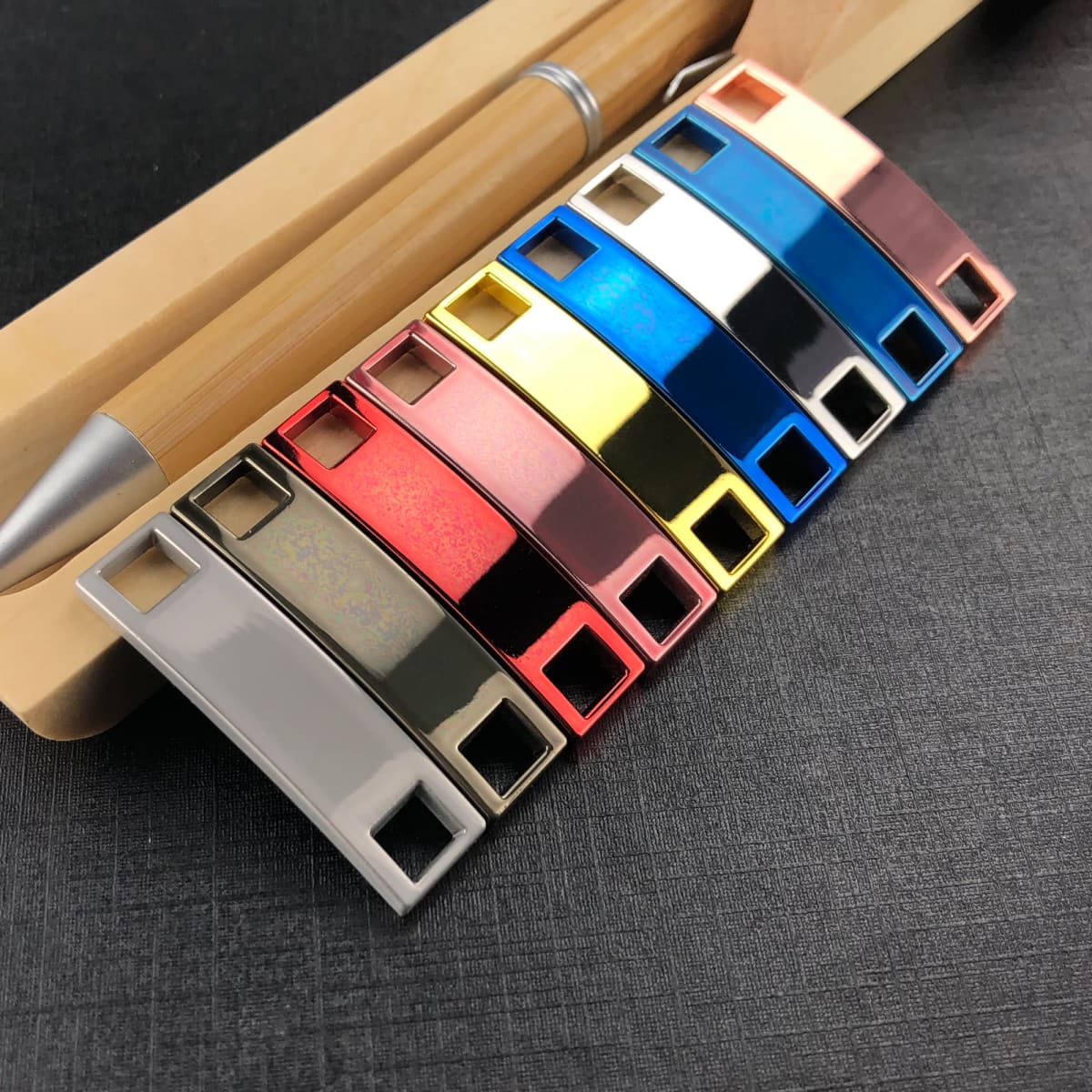 A collection of colourful luxury shoelace charms displayed alongside a pen on a textured surface.