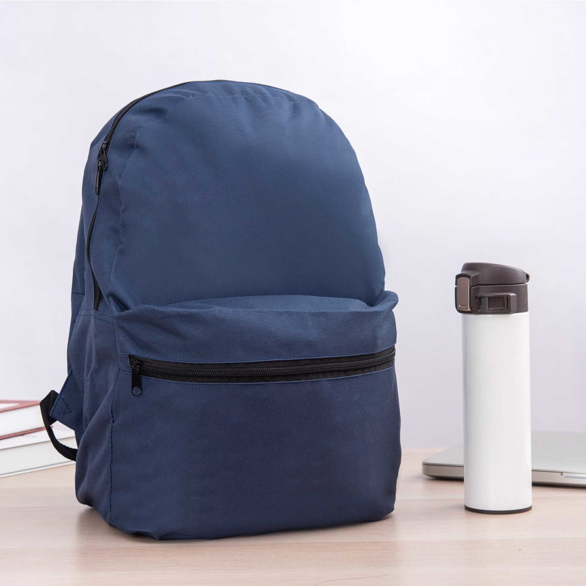 A navy blue backpack with a front pocket sits next to a white drink bottle on a wooden surface.