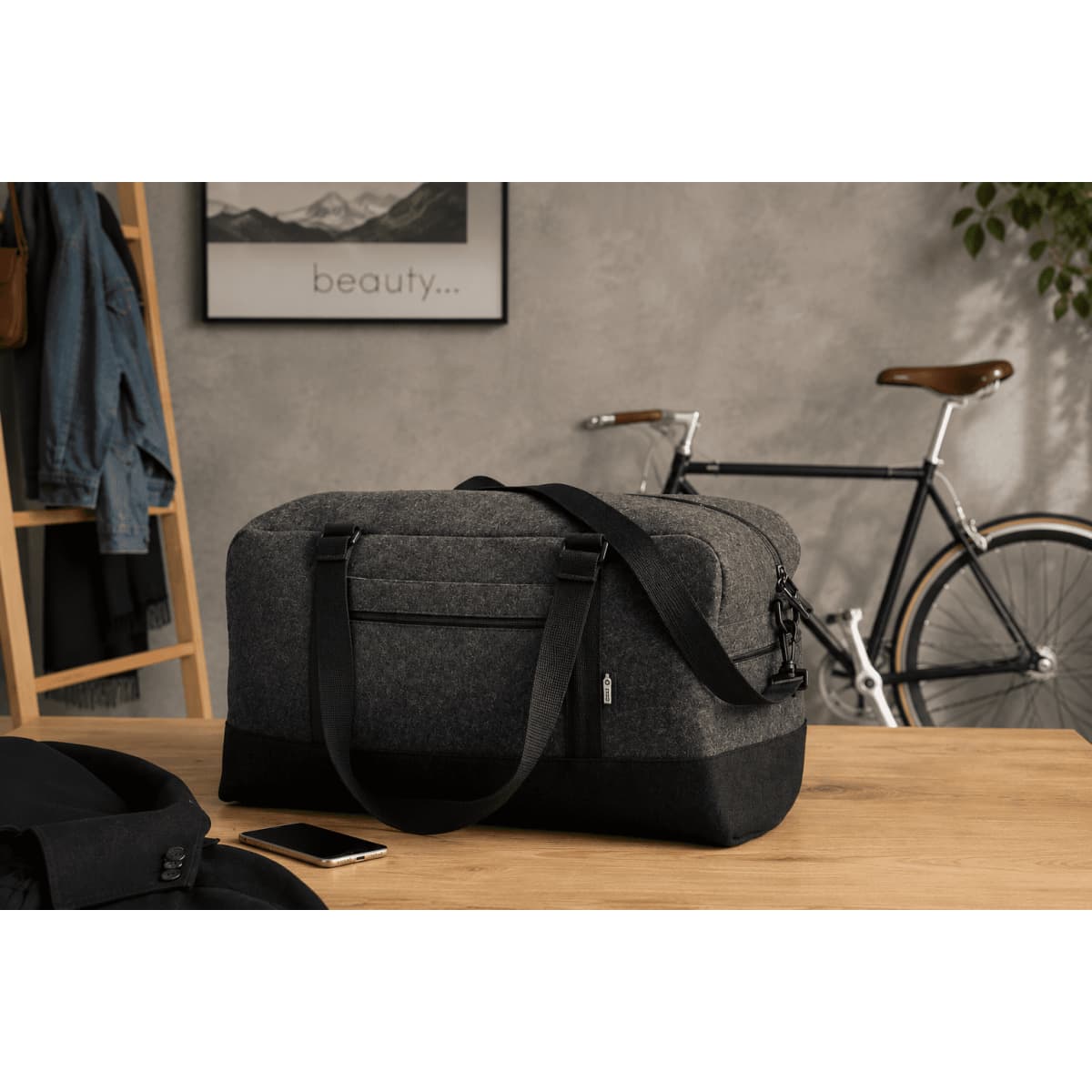 A grey and black duffle bag with sturdy handles, positioned on a wooden table beside a bike and a jacket.