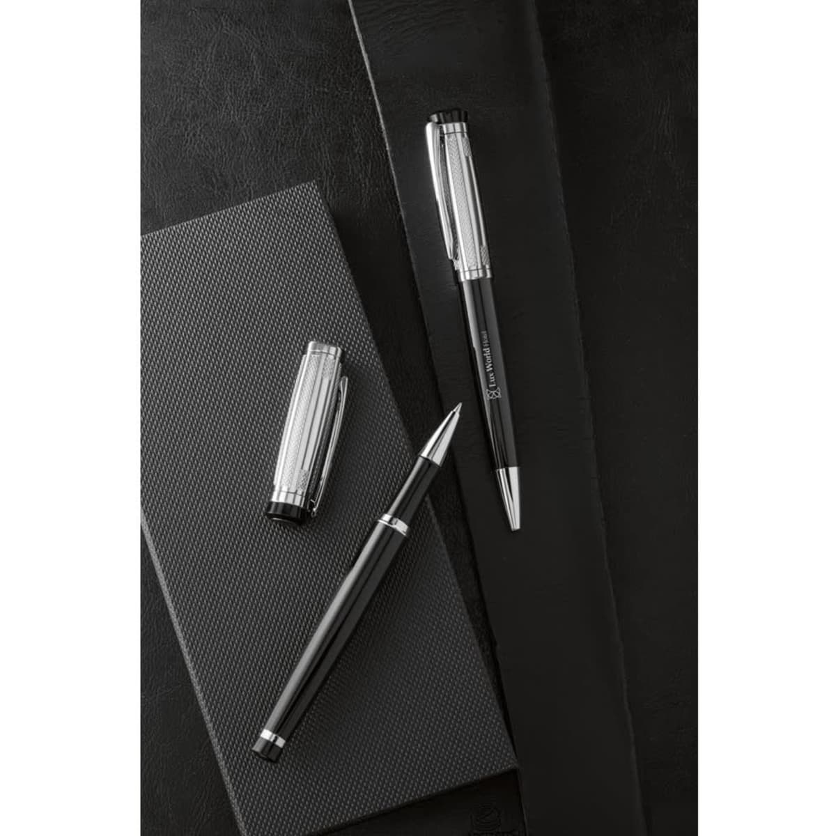 A black metal rollerball pen and a ballpoint pen set on a textured black notebook, featuring a clip and logo.