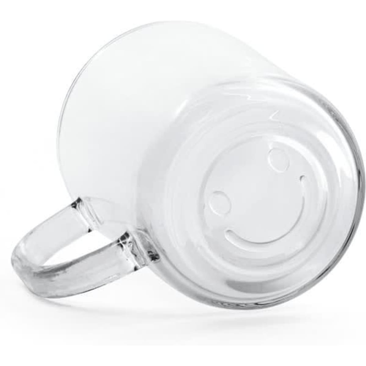 A glass mug with a clear design and a smiley face on the base, positioned on its side.