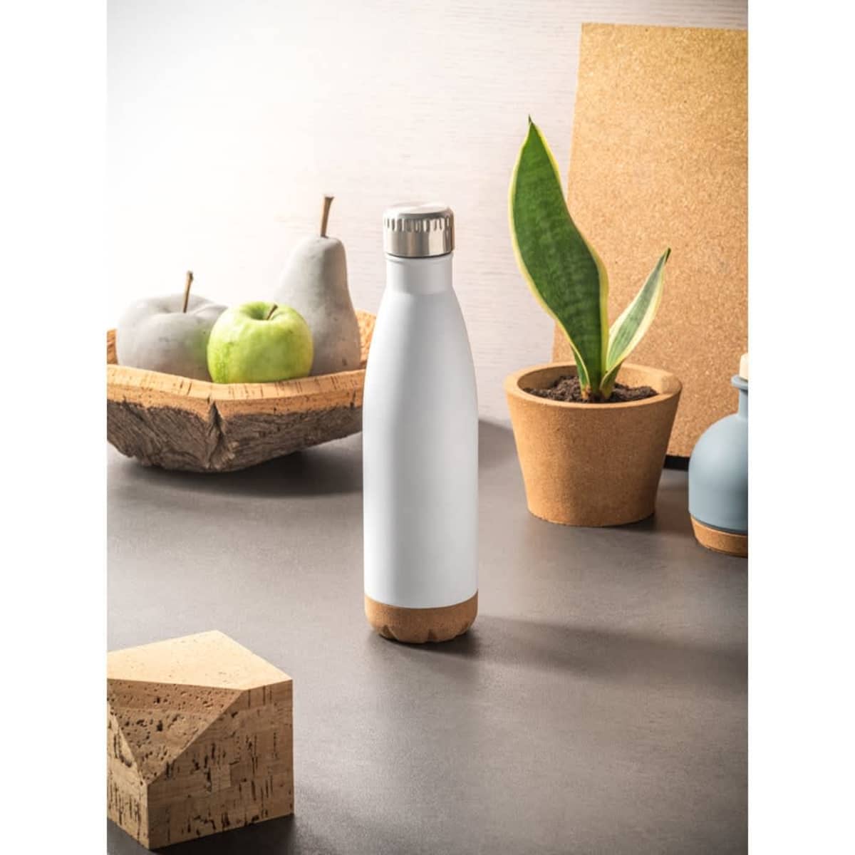 A drink bottle with a white stainless steel body and cork base, surrounded by decorative items and plants.