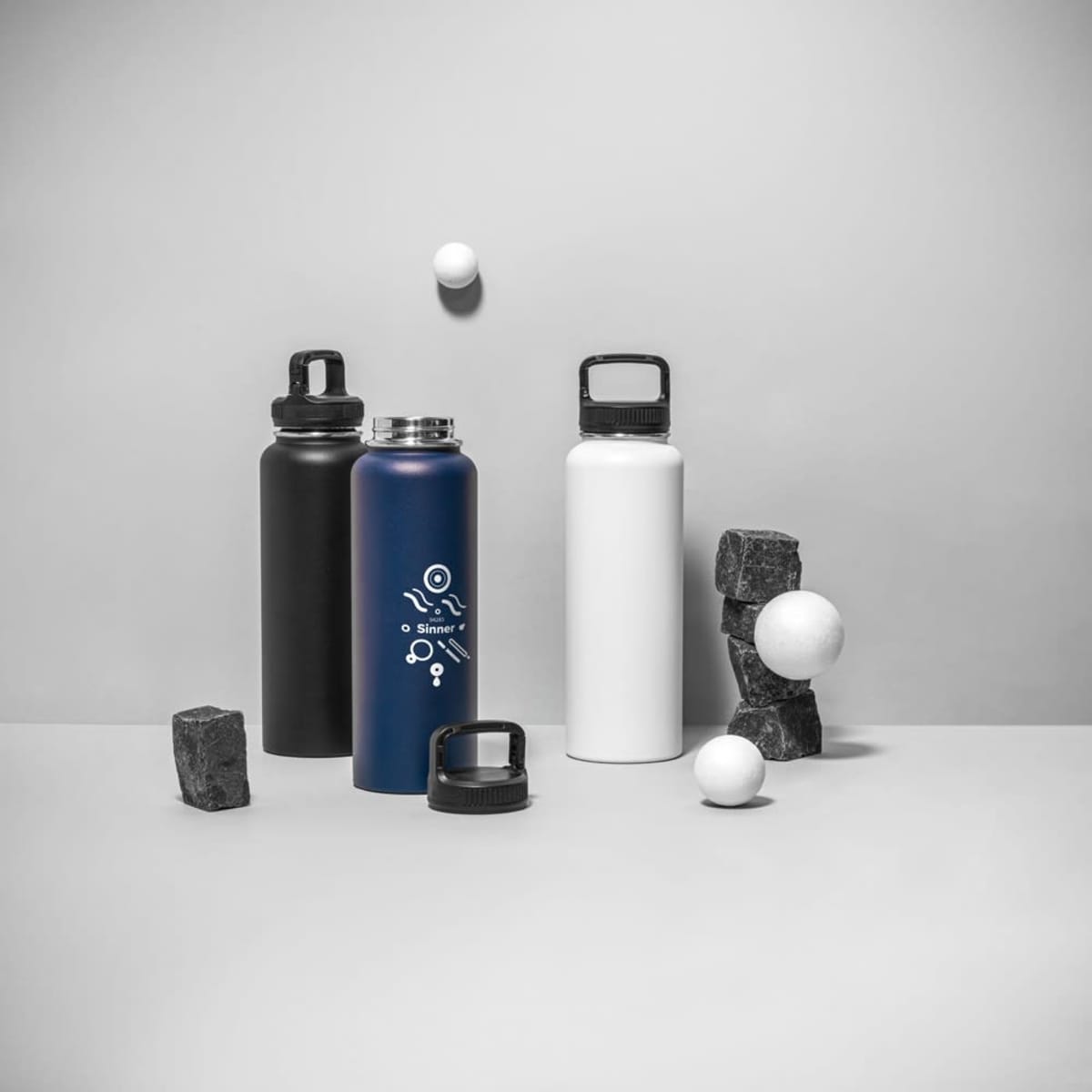 A drink bottle collection featuring a blue bottle, a black bottle, and a white bottle, with a logo on the blue.