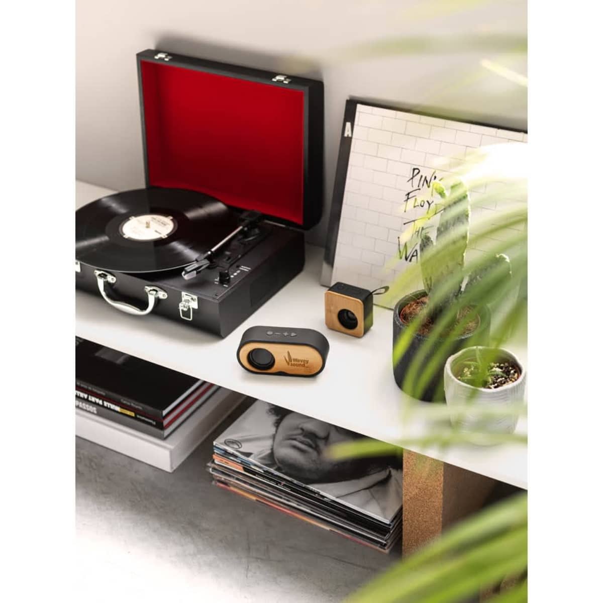 A portable bamboo and recycled ABS speaker in natural and black tones sits beside a vintage record player on a shelf.