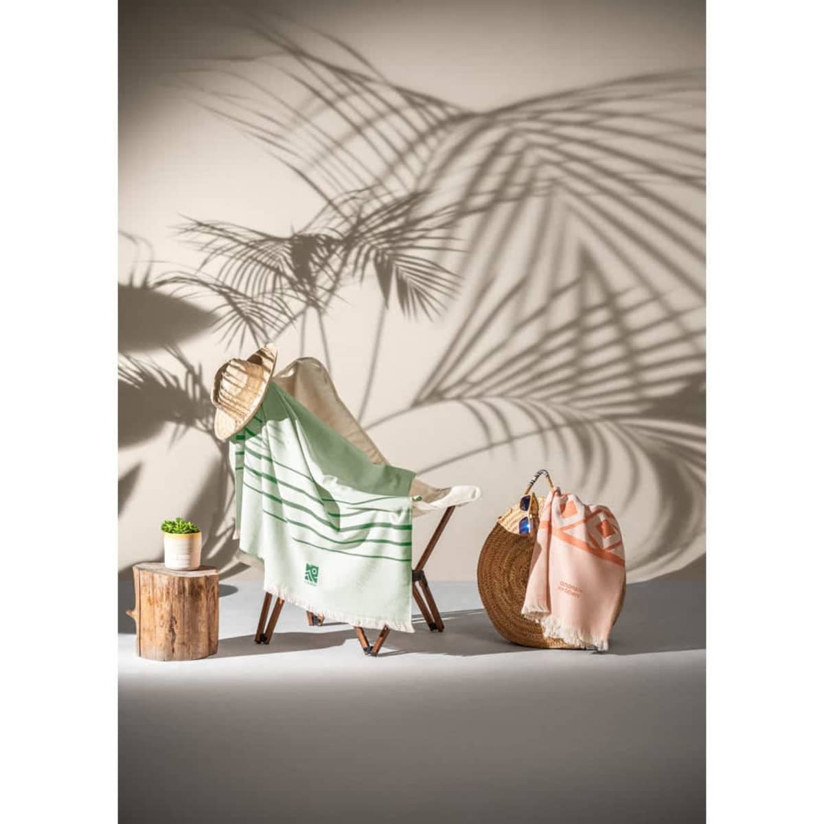 A green and cream striped towel draped over a chair, with a peach towel nearby, against a shadowy palm backdrop.