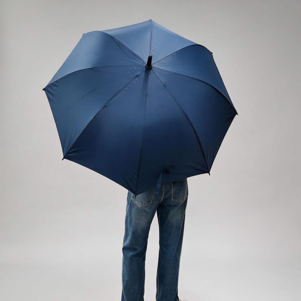 A navy blue umbrella with an automatic opening mechanism, held by an individual wearing jeans.
