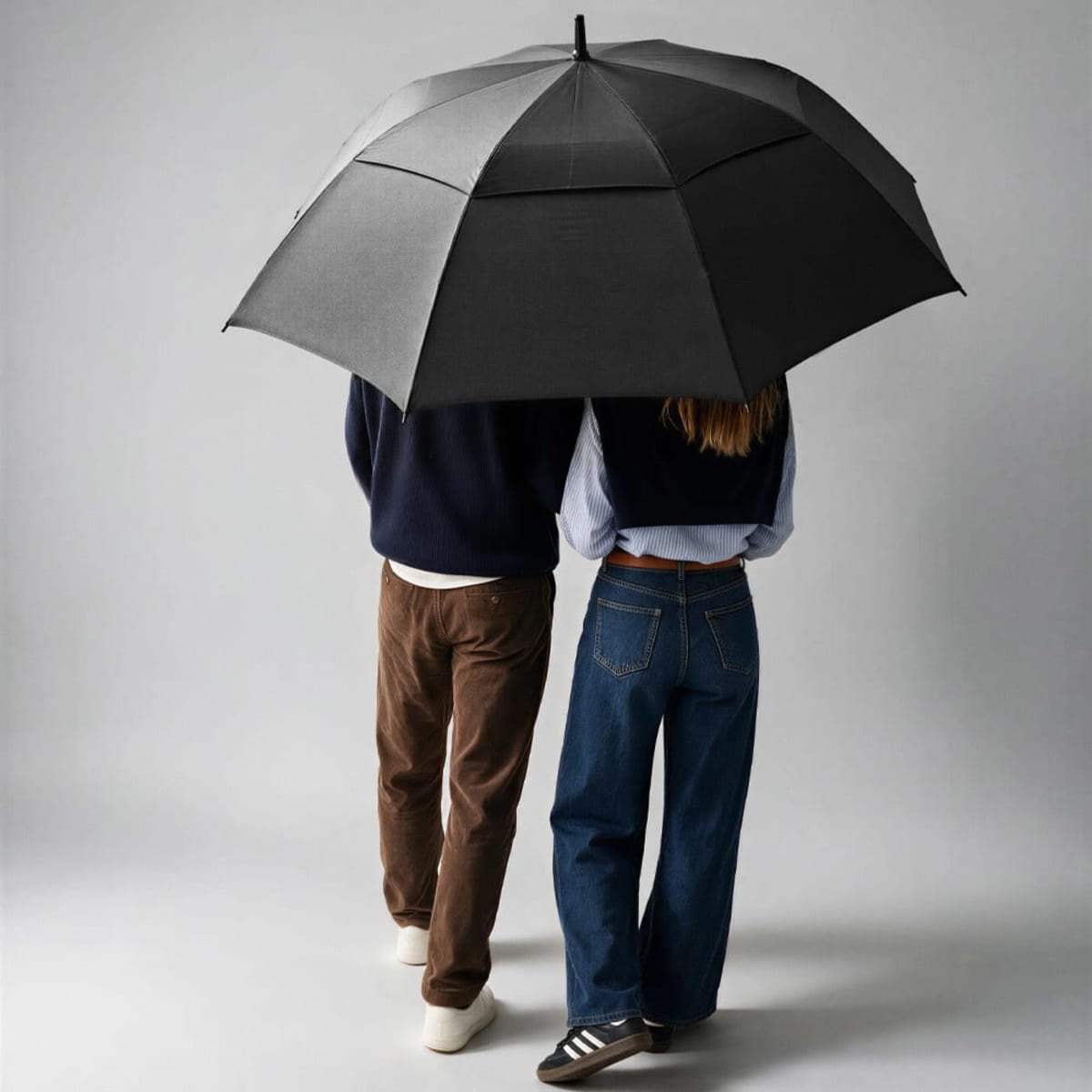 A black golf umbrella with a storm-proof design, featuring automatic opening, held by two people walking together.