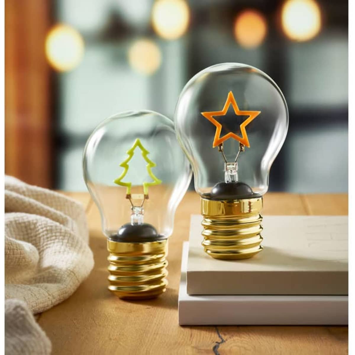 Two decorative light bulbs on a wooden surface, one with a green tree design and the other with an orange star design.