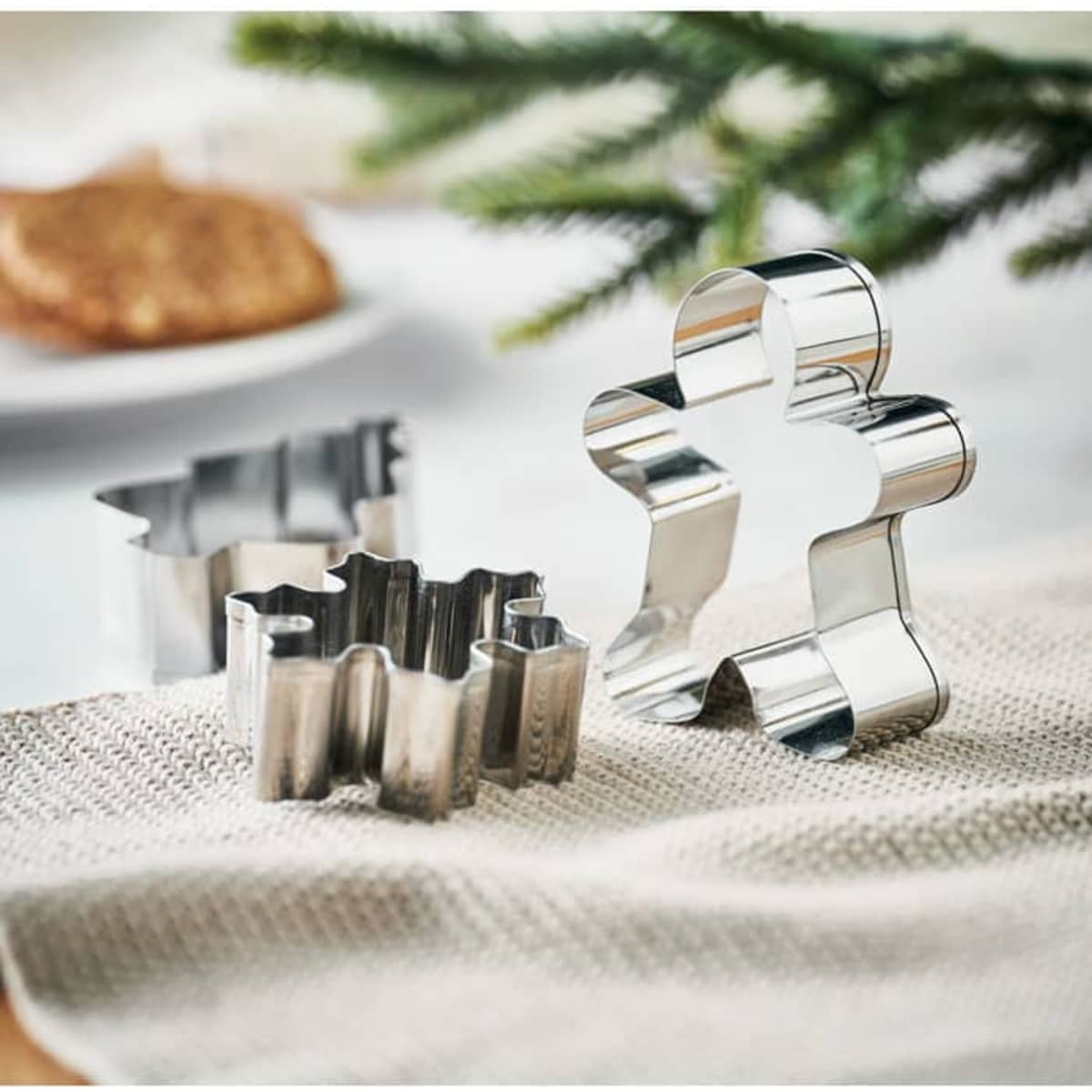 Three stainless steel cookie cutters in various shapes, including a gingerbread man, placed on a textured cloth.