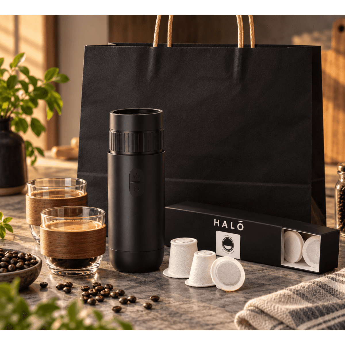 A black drink bottle, coffee pods, two glasses, and a black bag, arranged on a tabletop with coffee beans.