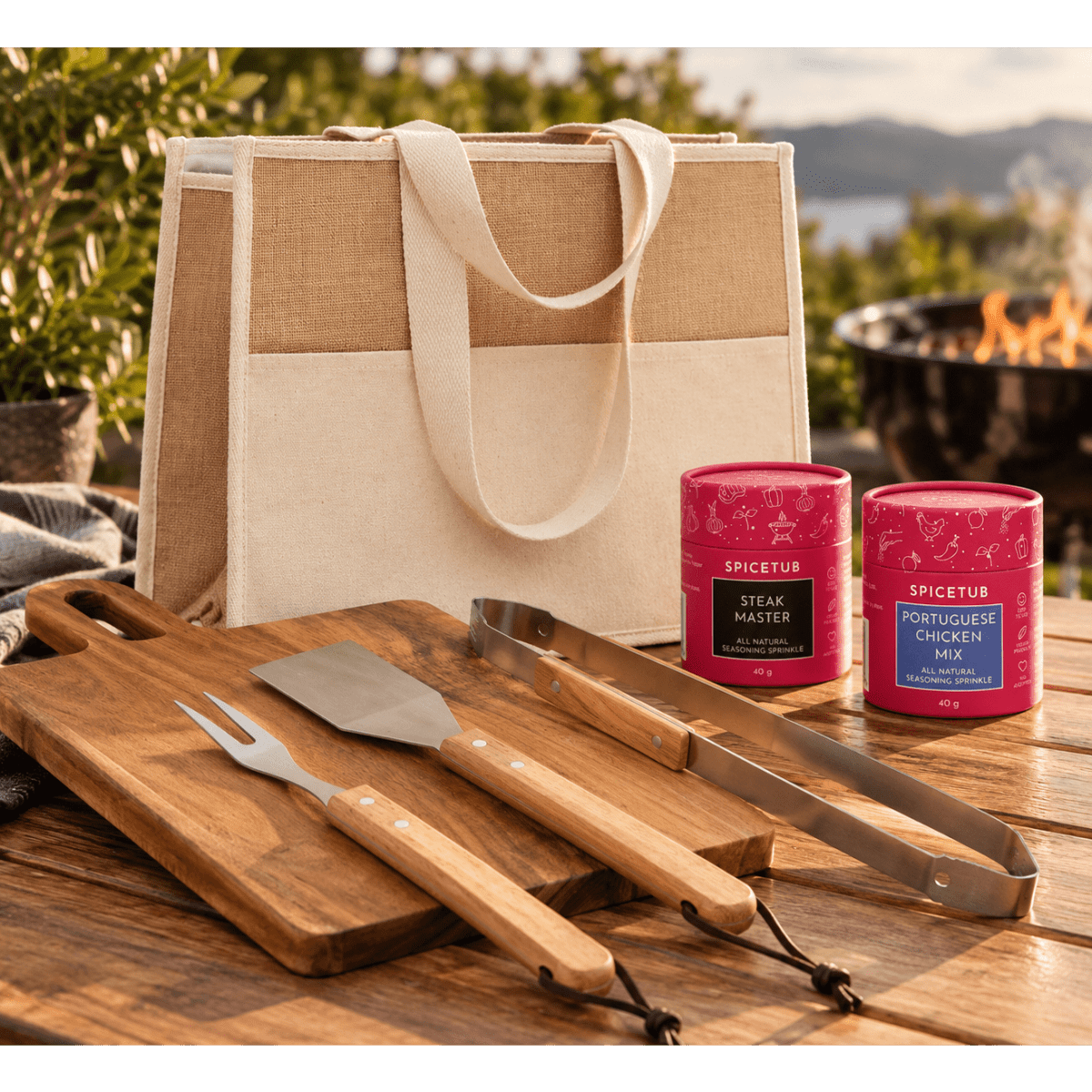 A canvas tote bag with two spice jars, a wooden chopping board, and barbecue utensils in natural wood tones.