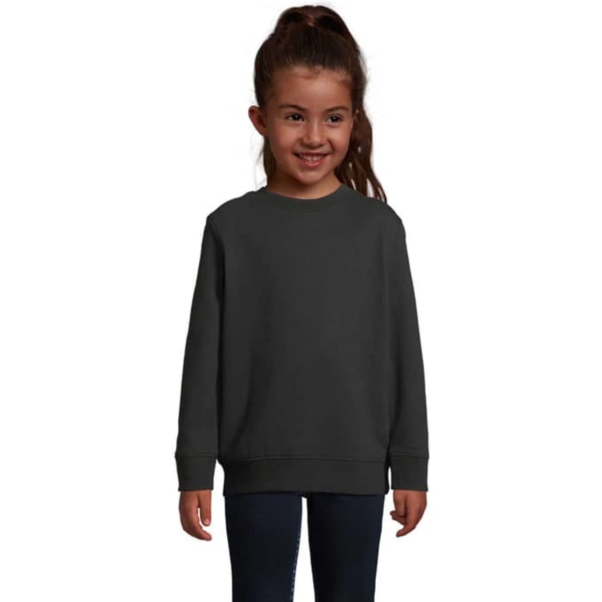 A child wearing a dark grey sweatshirt, smiling and standing against a white background. The sweatshirt has a logo.