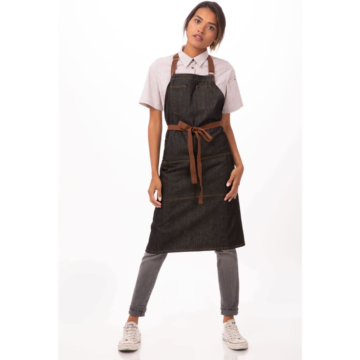 A denim apron in dark blue with brown straps, featuring a front pocket and a fitted design.