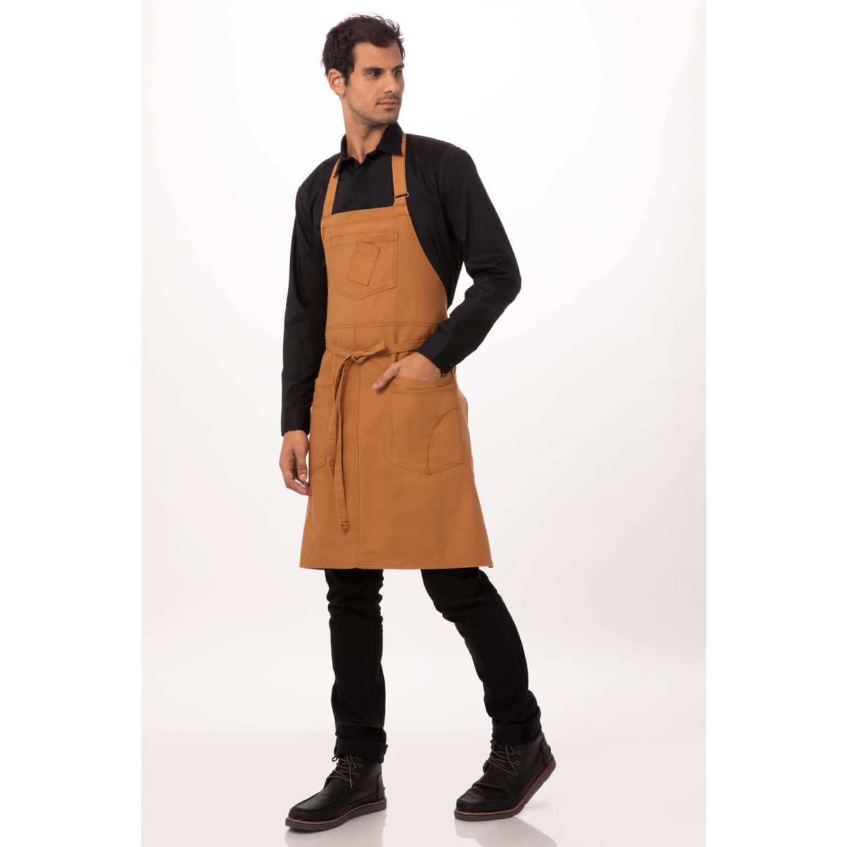 A tan bib apron worn by a model, featuring pockets and an adjustable neck strap. The model is dressed in black.