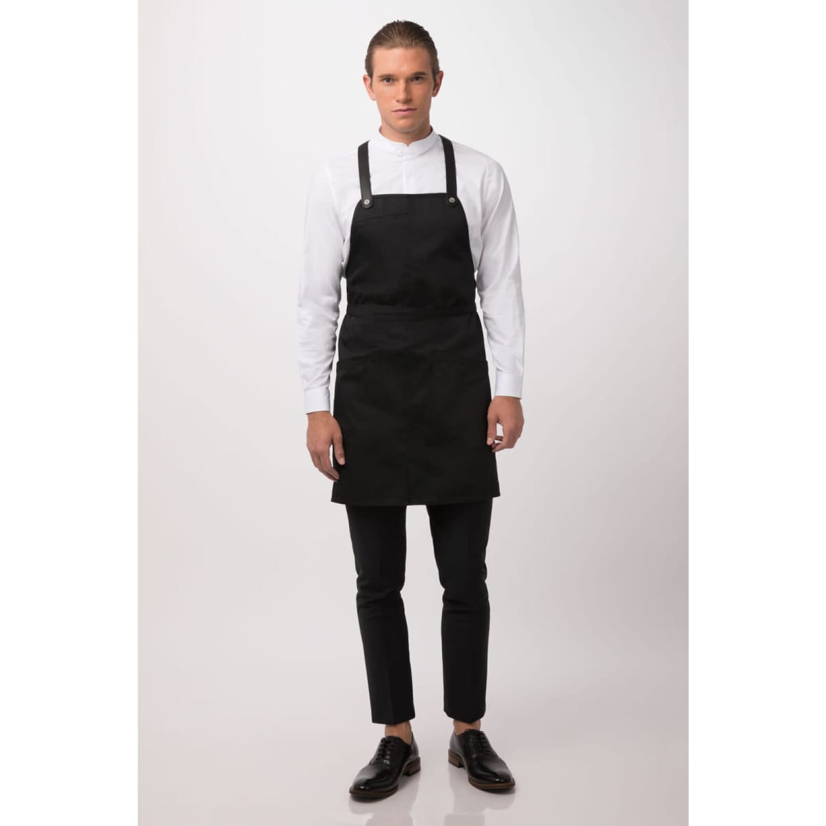A black Largo Bib Apron is worn by a model, paired with a white shirt and black trousers. The apron features straps and has a logo.