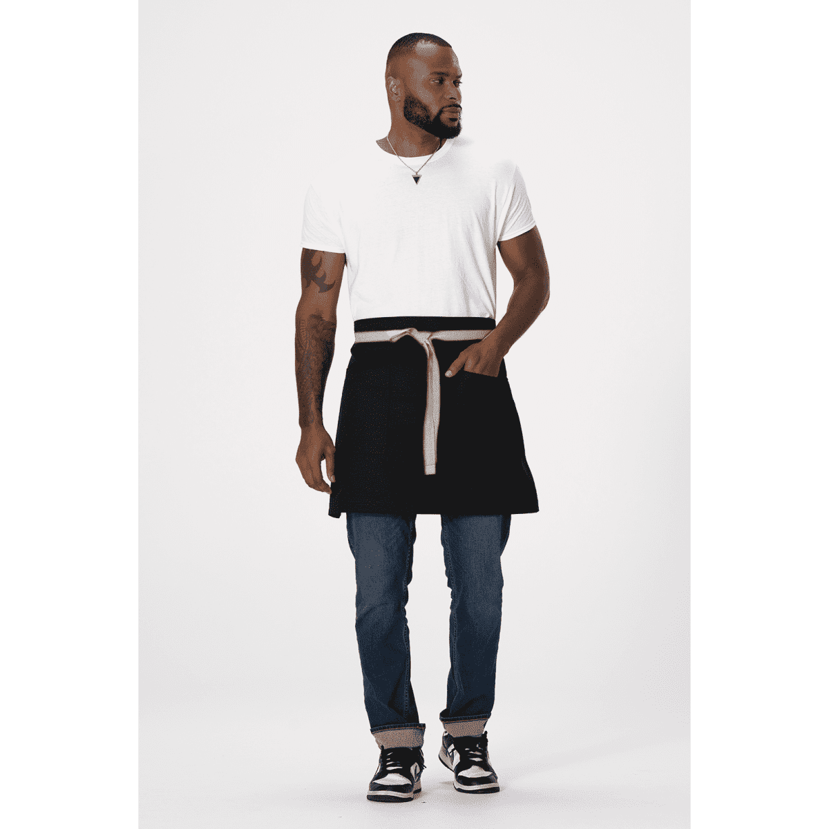 A man wearing a black Lockharte waist apron over a white T-shirt, paired with blue jeans and sneakers. The apron features a logo.