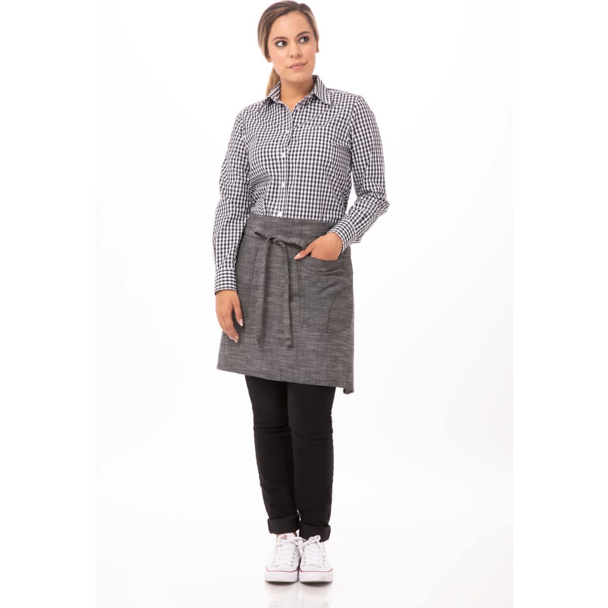A woman stands wearing a grey half bistro apron over a checked shirt and black pants, featuring a pocket and a tie waist.
