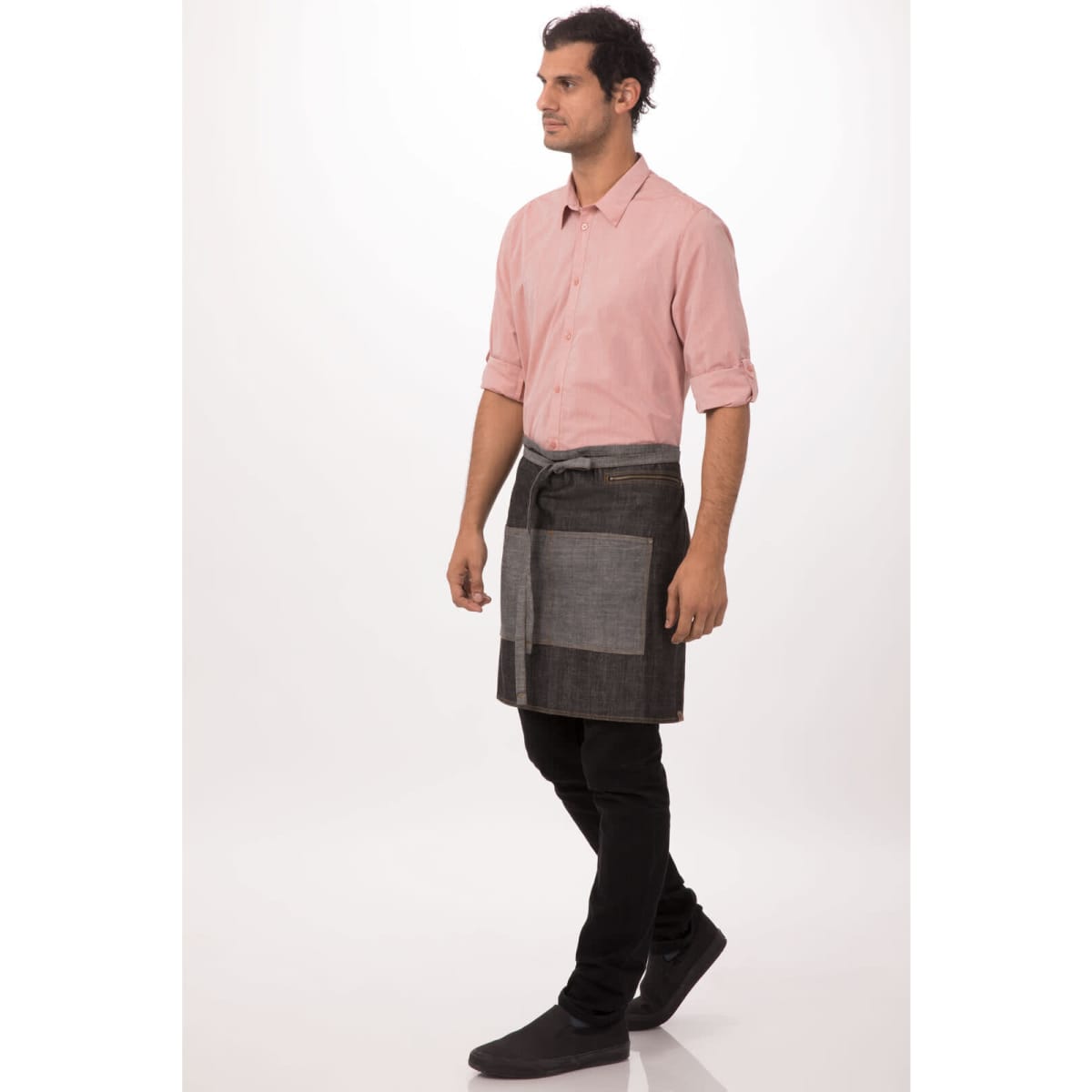 A man wearing a grey and dark grey Manhattan Half Bistro Apron over a light pink shirt and black pants, standing sideways.