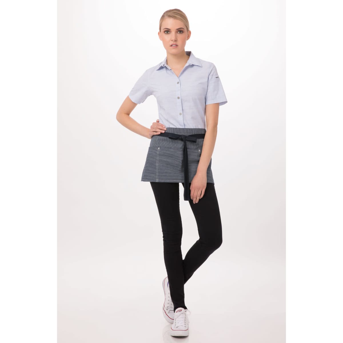 A woman is wearing a grey waist apron over a light blue shirt, paired with black leggings and white shoes.