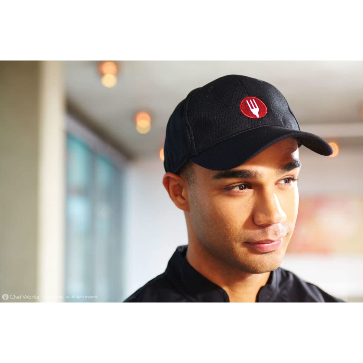 A black baseball cap with a logo, worn by a person in a restaurant setting.