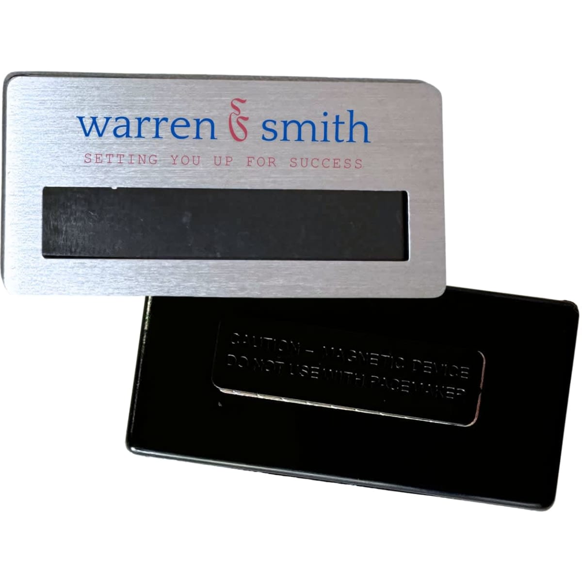 A silver magnetic staff badge with a smooth finish and a black backing. Features a logo.