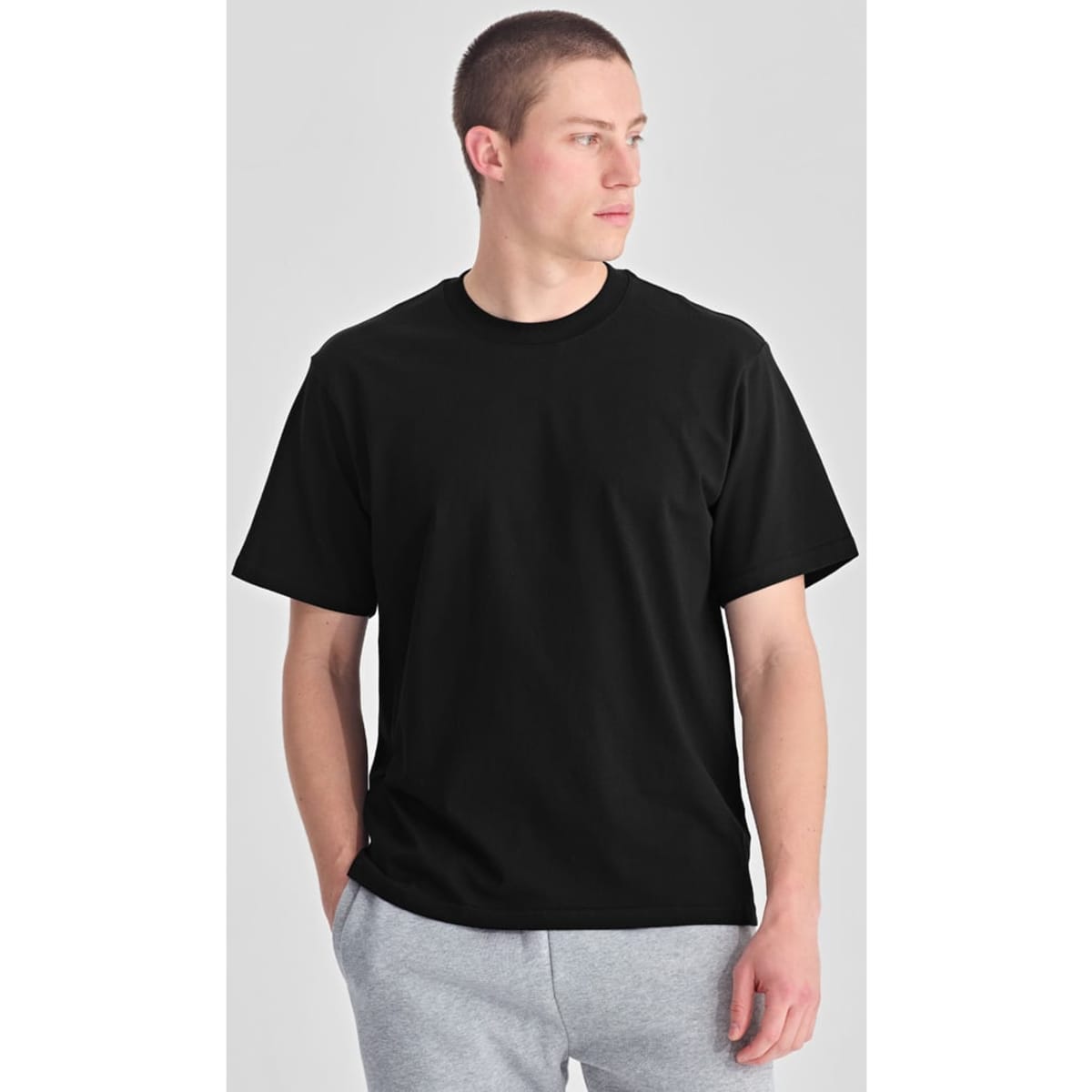 A black box tee worn by a model standing with hands in pockets, featuring a simple design and a relaxed fit.