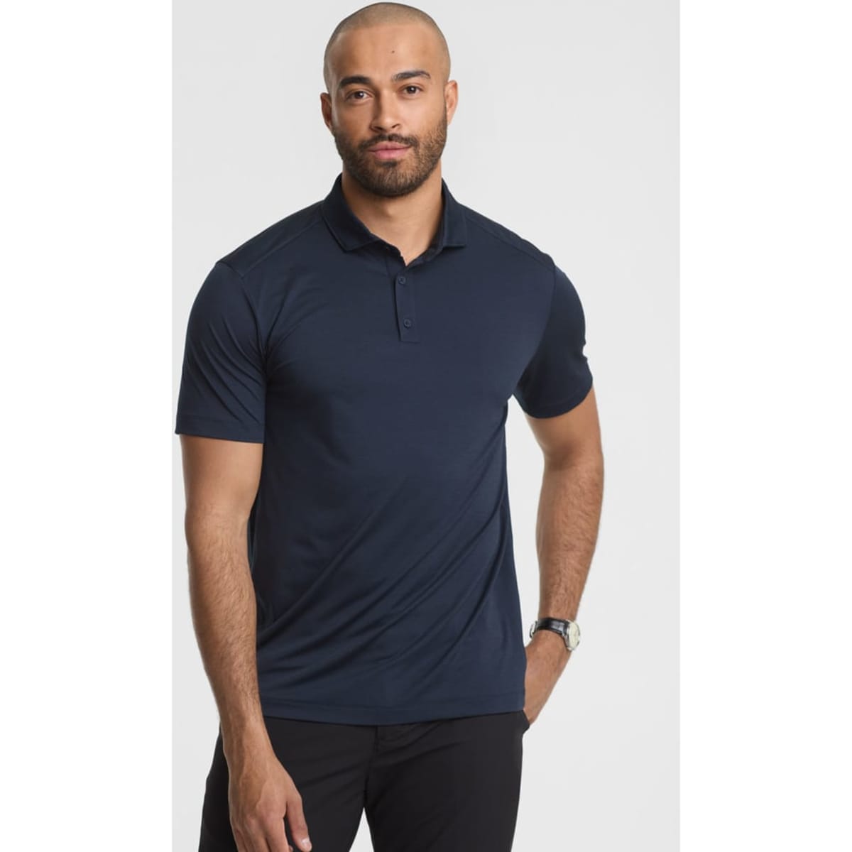 A man stands wearing a navy blue short sleeve polo shirt, featuring a collar and a logo.