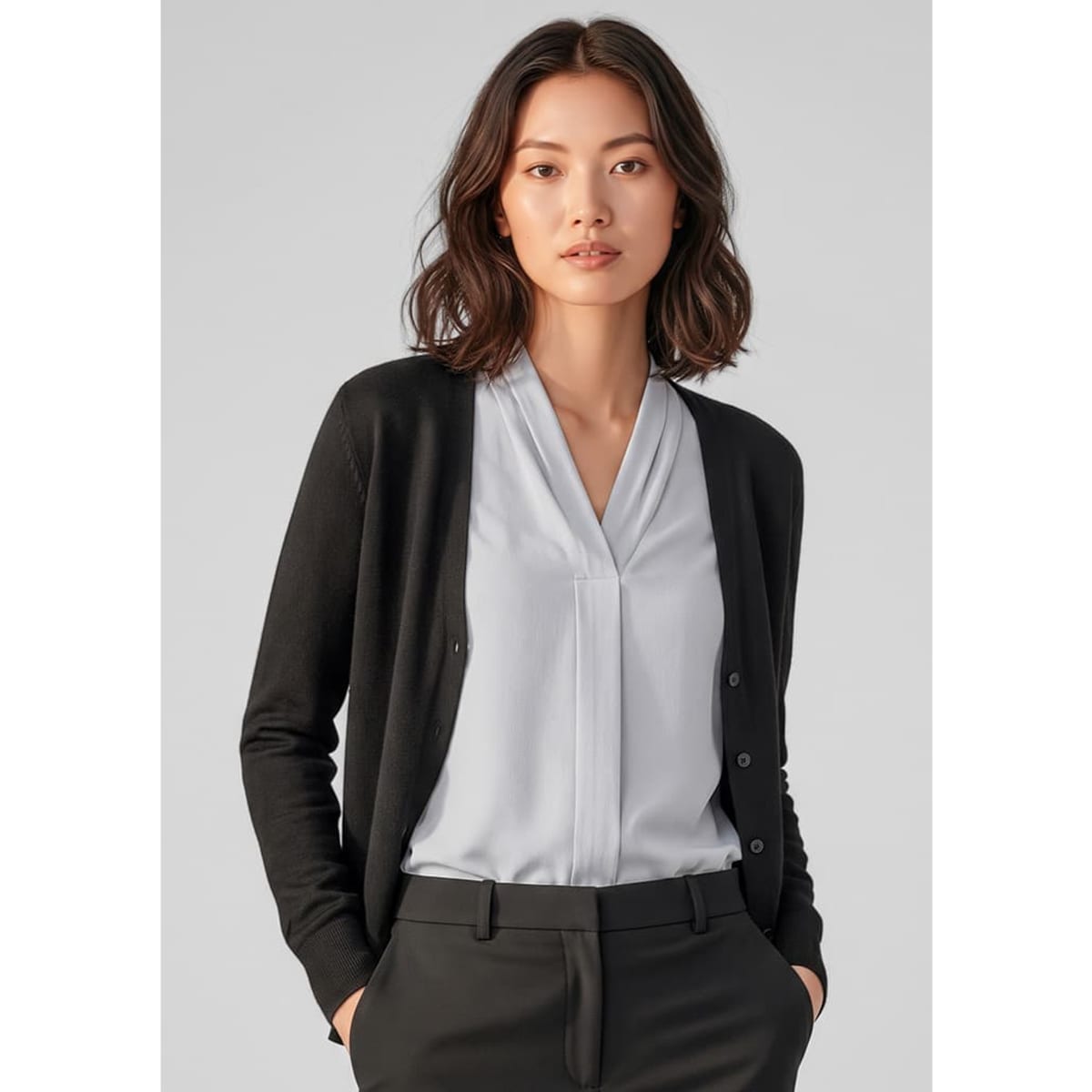 A black knit cardigan worn over a light blue blouse, styled with tailored black trousers. The model has shoulder-length hair.
