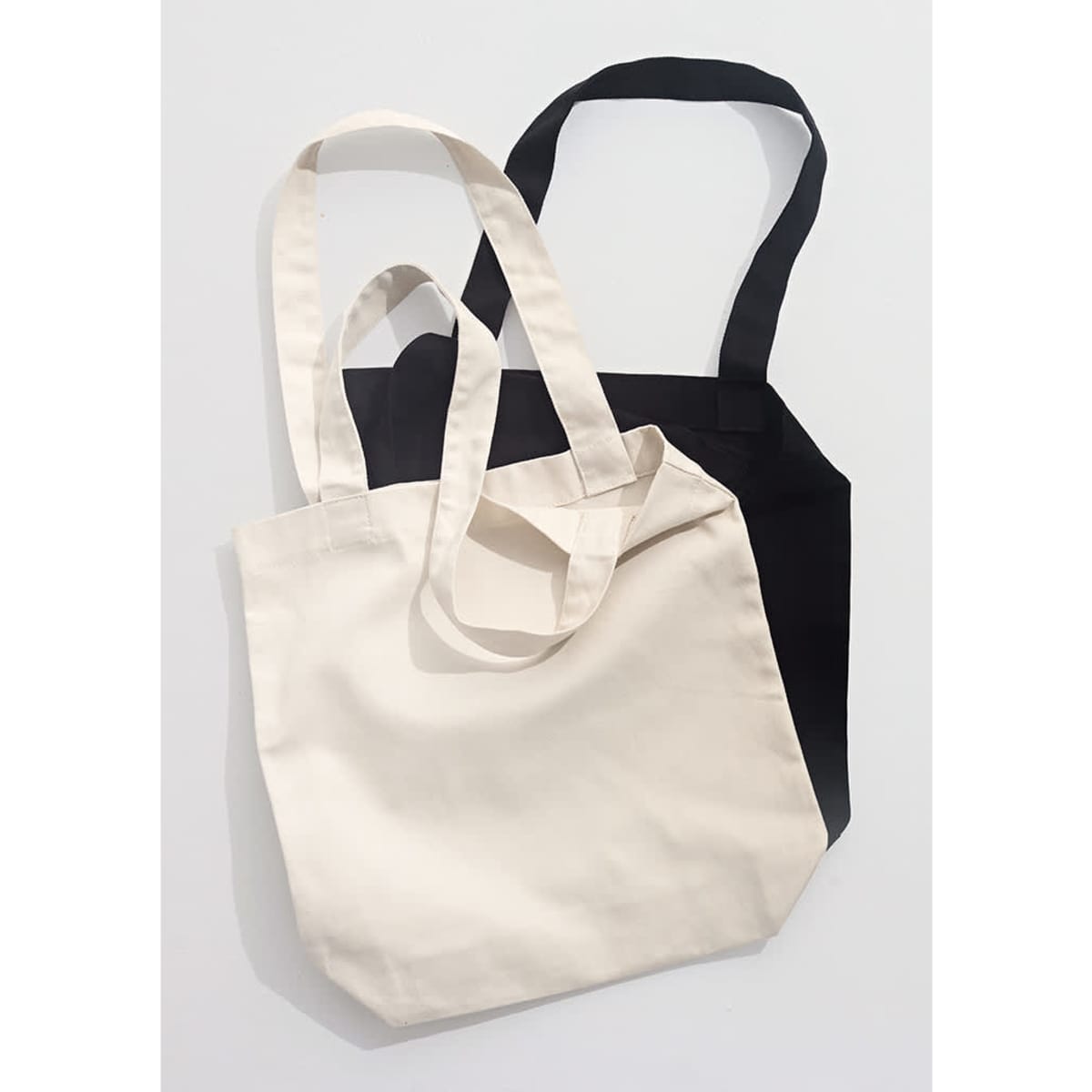 Two canvas tote bags, one in cream and one in black, featuring long handles and a simple design.