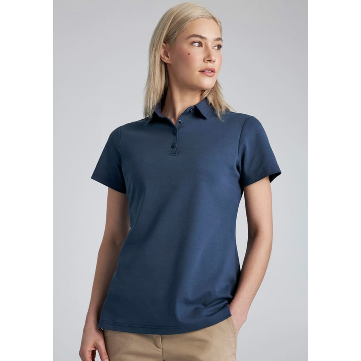 A woman models a navy blue short sleeve polo shirt with a collar and a logo on the chest.