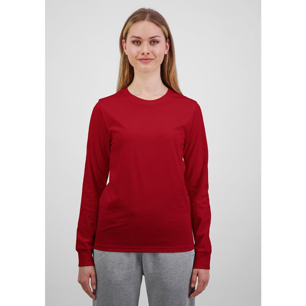 A long sleeve women's tee in bright red, displayed by a model in grey trousers, featuring a logo.