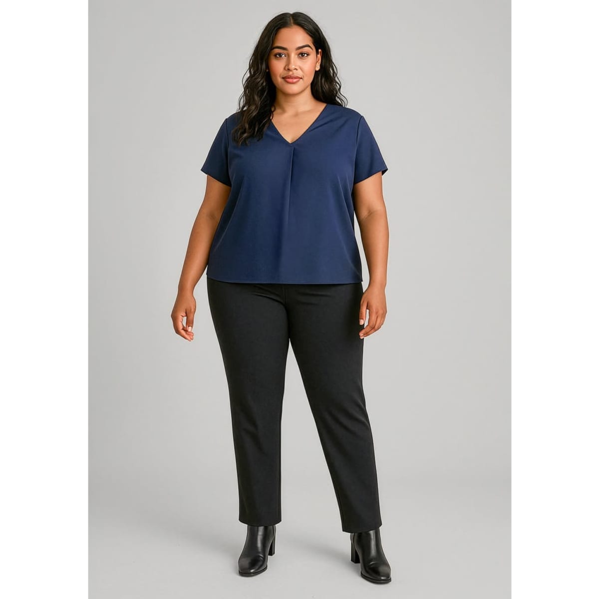 A model wearing a navy top and black mid-rise pull-on pants, with sleek black boots. The outfit features a subtle logo.