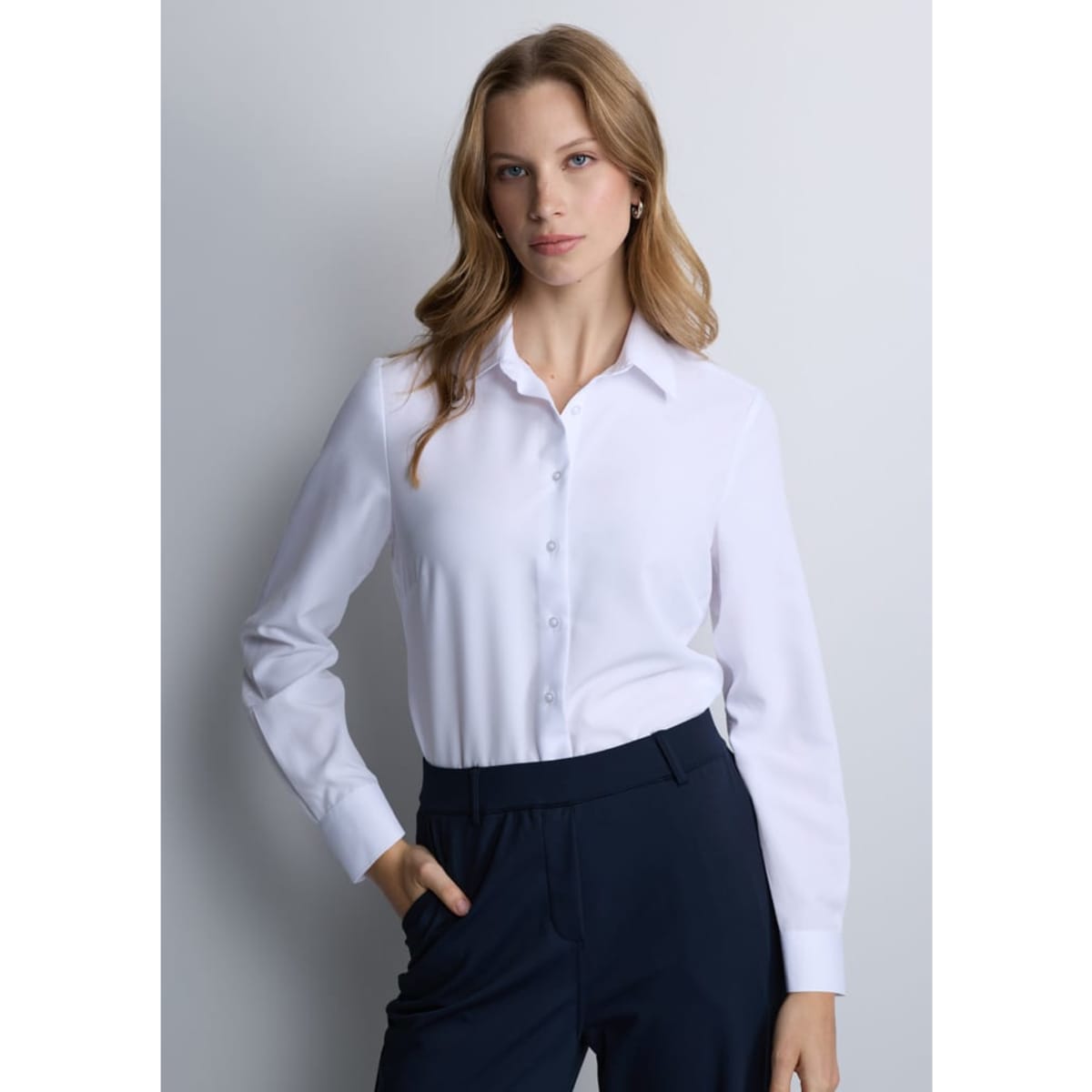 A women's long sleeve shirt in white with a button-up front and a collar, paired with dark pants.