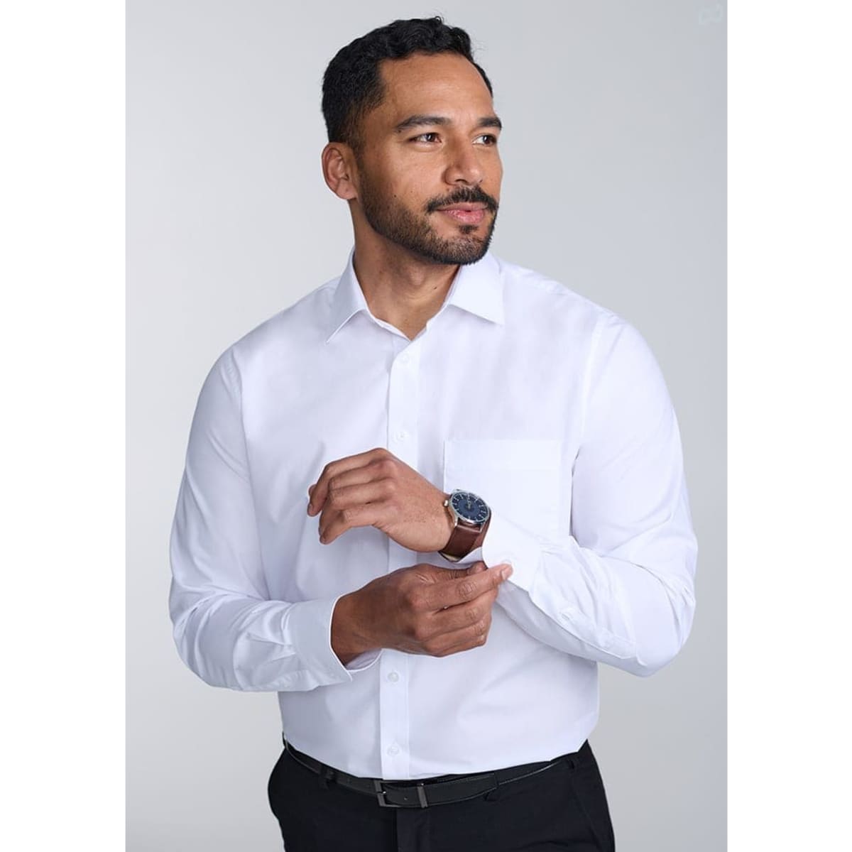 A classic fit long sleeve shirt in white, worn by a man adjusting his cuff, featuring a watch on his wrist.