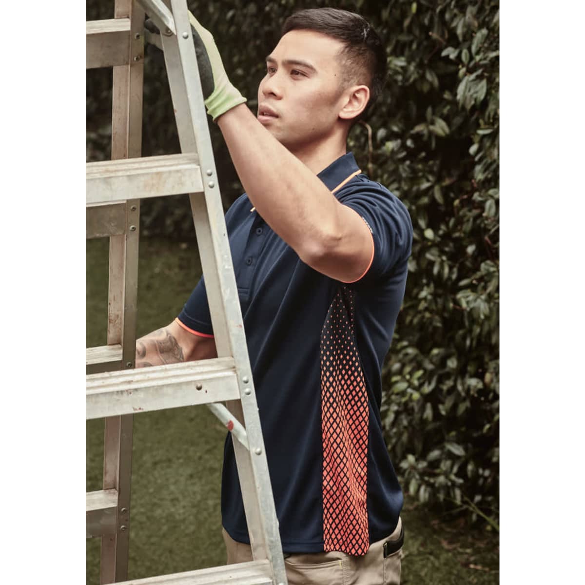 A man in a navy blue short sleeve polo with an orange and white design on the side, climbing a ladder outdoors.