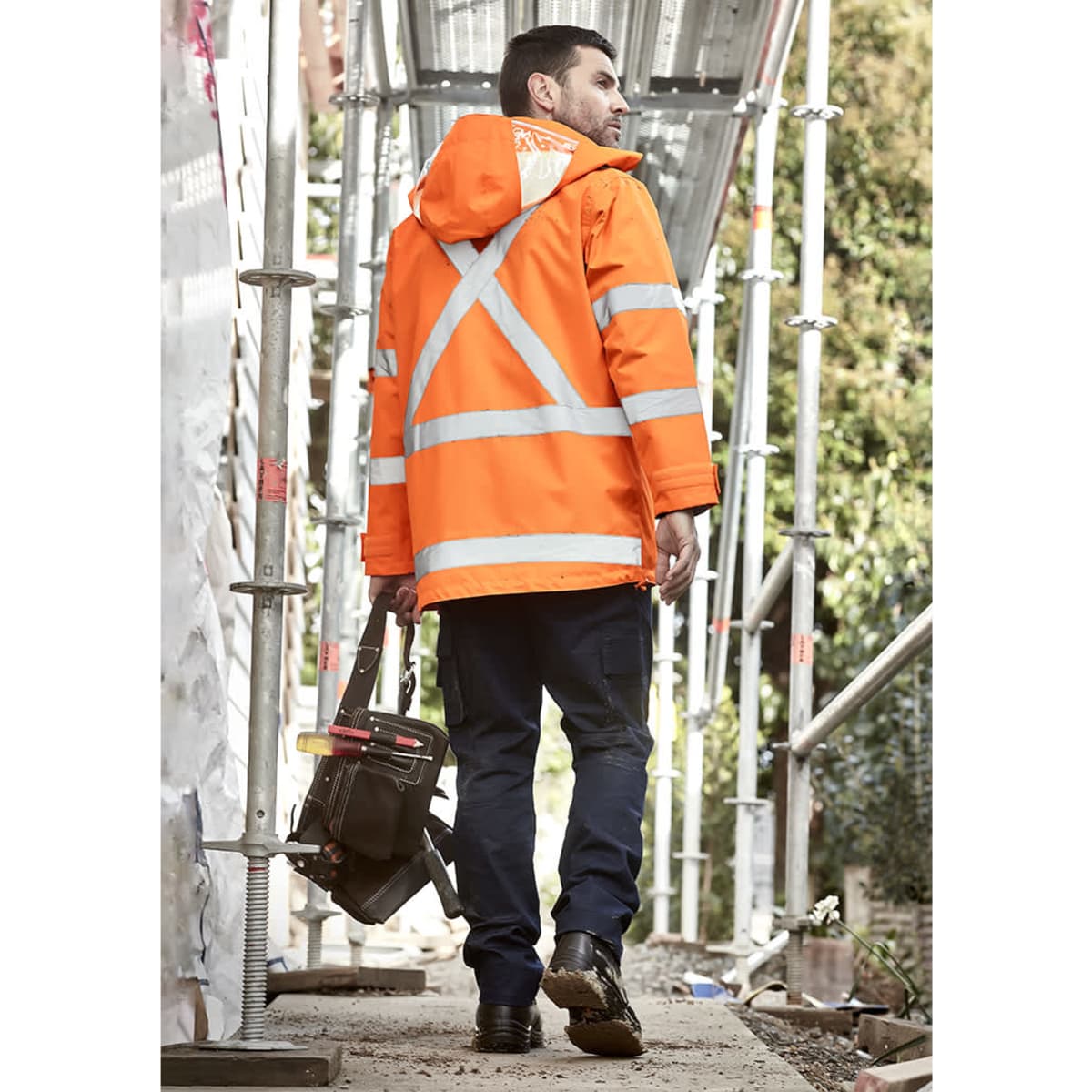 A waterproof orange jacket with reflective strips, worn by a man carrying a tool bag, against a construction backdrop.