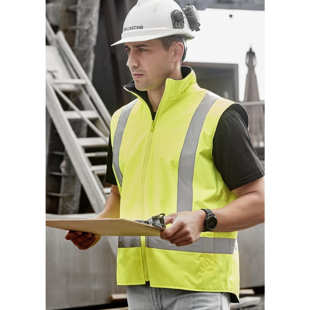 A man wearing a bright yellow waterproof reversible vest with reflective stripes, holding a clipboard.