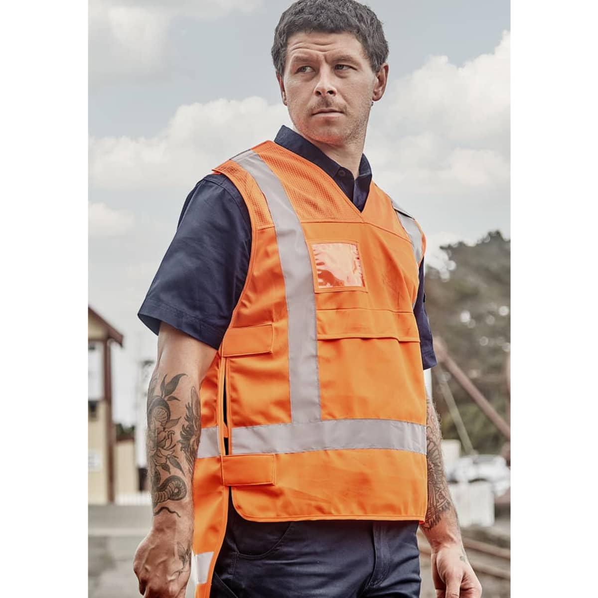 A unisex hi-vis safety vest in bright orange, featuring reflective strips and pockets, shown on a model.