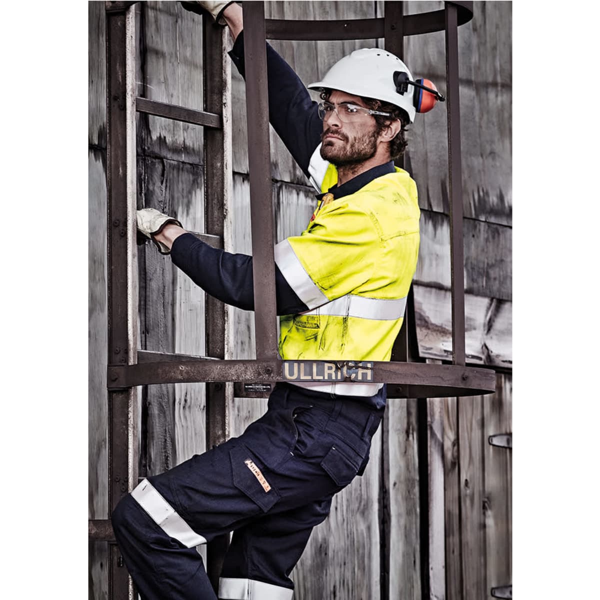 A man wearing a hi-vis yellow and navy work shirt, climbing a metal ladder, with protective gear and glasses.