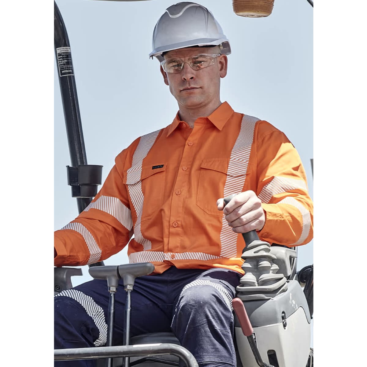 A man wearing an orange hi-vis shirt with segmented reflective tape operates machinery while wearing a white hard hat and safety glasses.