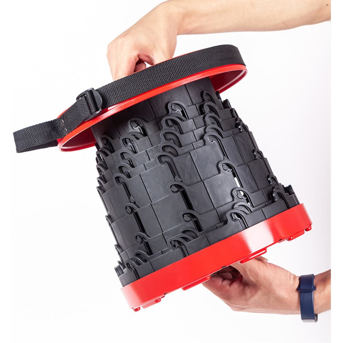 A red and black telescopic stool with a handle, held by a person, showcasing its collapsible design.