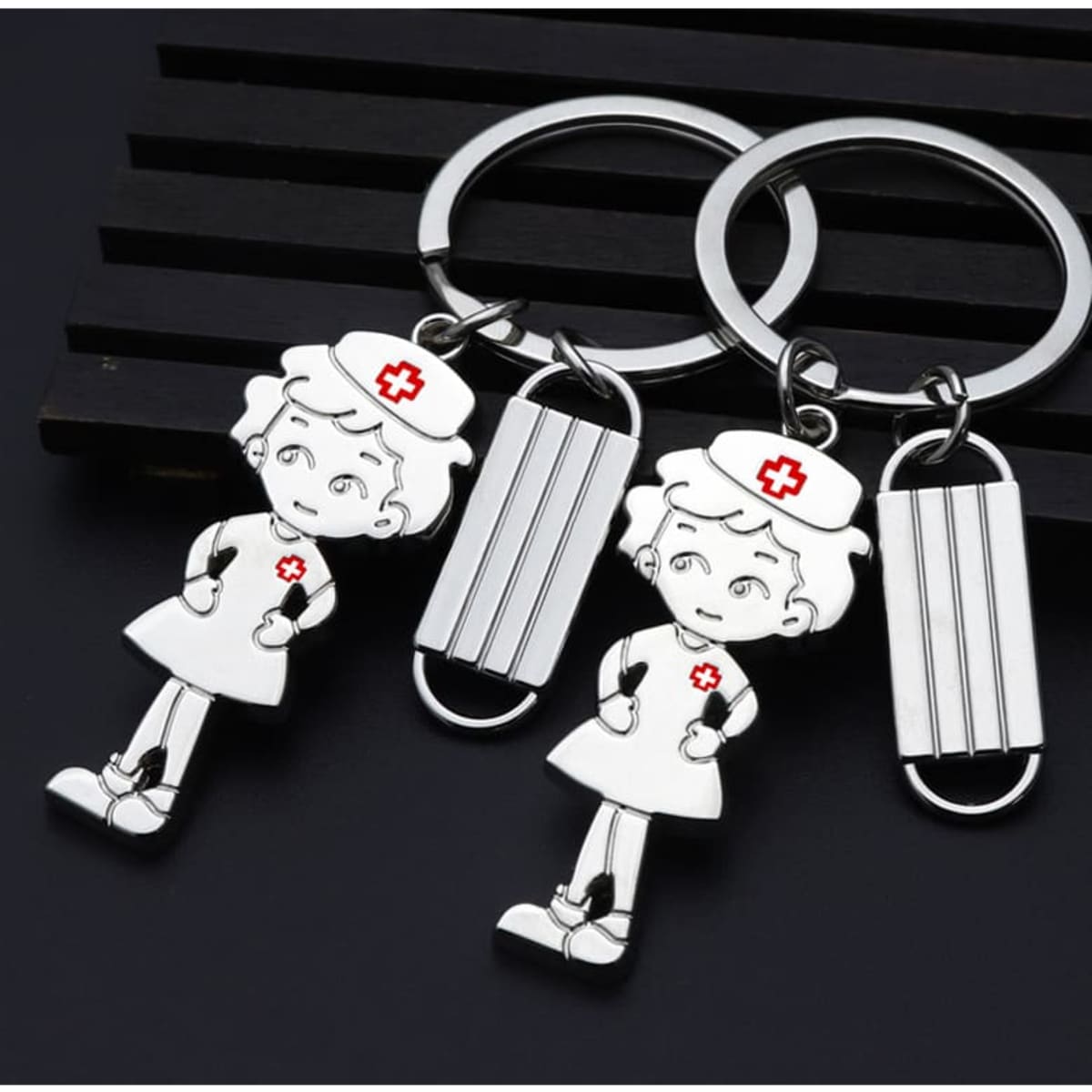 A silver keychain featuring a nurse figure and a mask shape, with a red cross detail on the nurse's uniform.