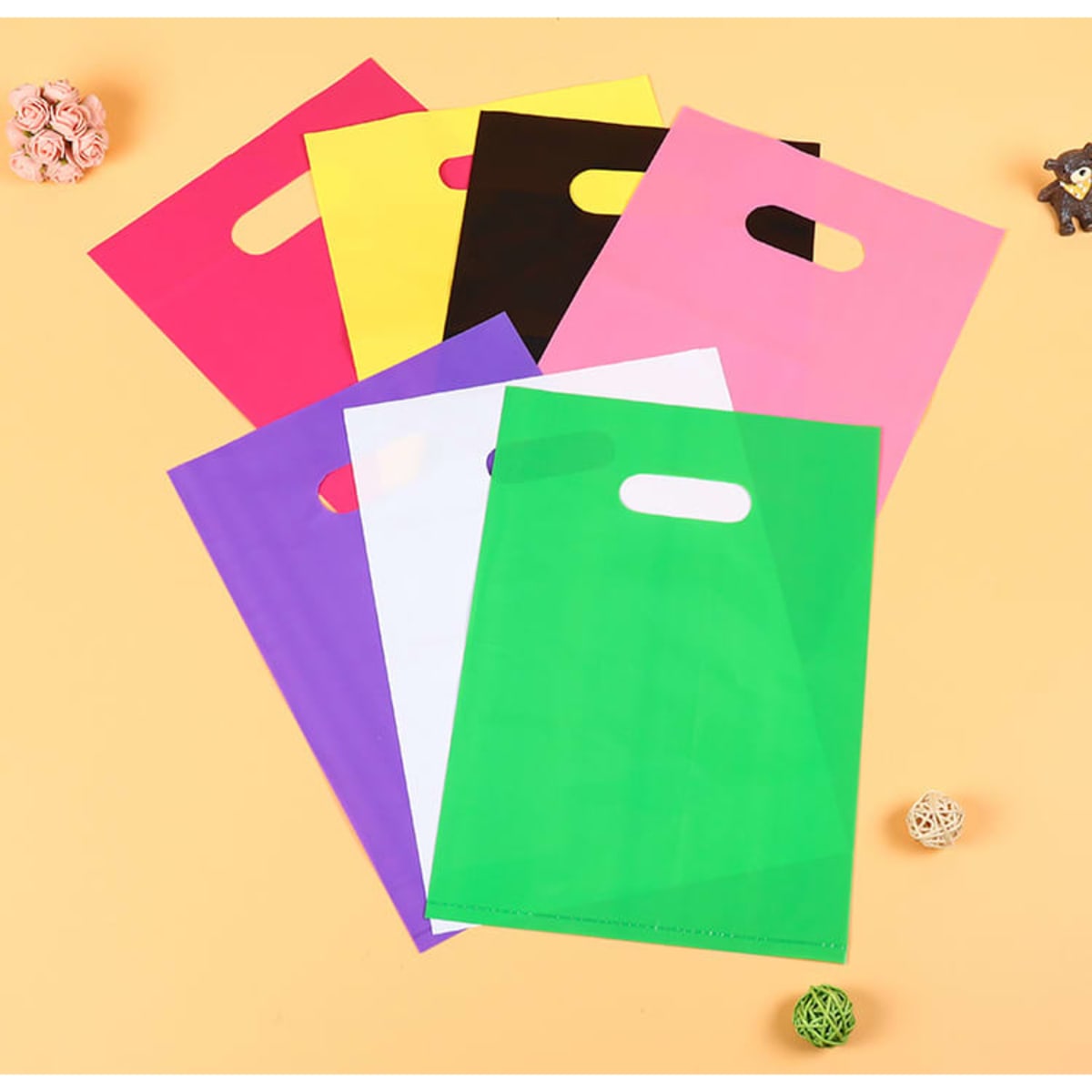 A collection of die cut plastic handle bags in pink, yellow, green, white, purple, black, and red, featuring various logos.