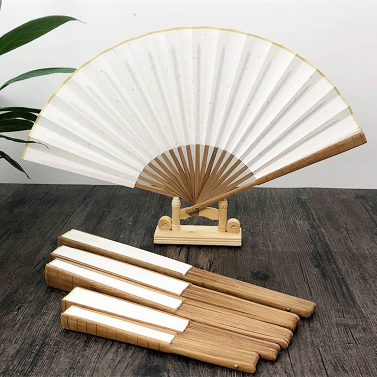 A folding fan with a wood frame and white fabric, displayed on a stand, alongside several matching wooden handles.