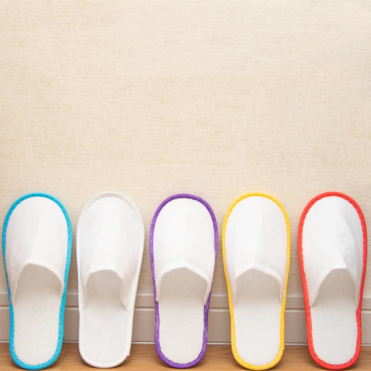 A set of five disposable hotel slippers in white, featuring colourful trim in blue, purple, orange, and yellow.