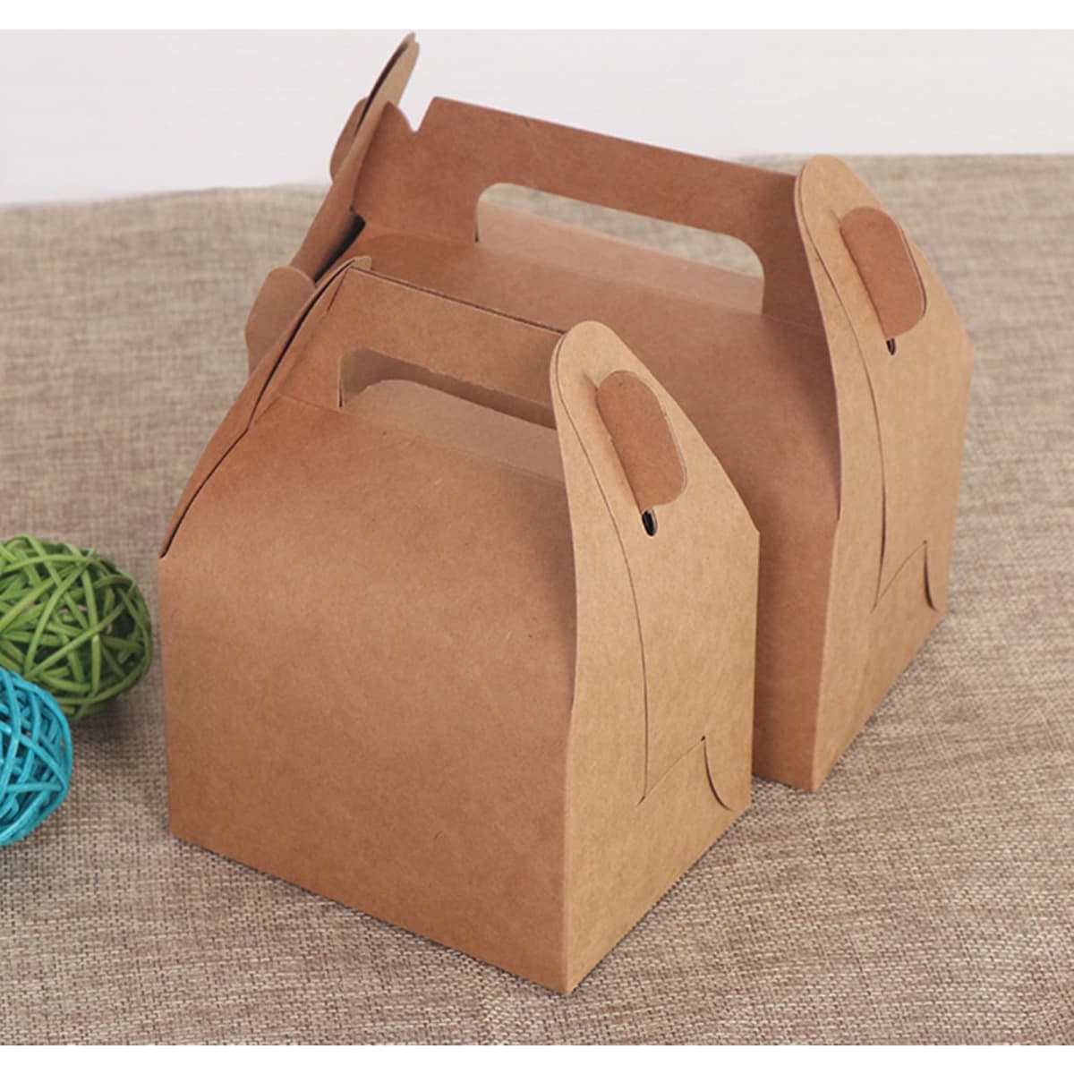 Two brown gable boxes made of kraft paper, featuring handles for easy carrying, on a textured surface.